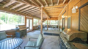 A covered outdoor area with wooden beams, a grill, tables, and chairs.
