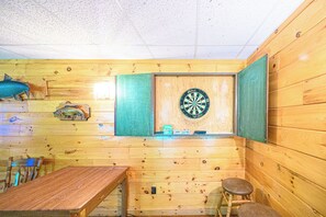 Interior de madeira com um alvo de dardos, uma mesa e cadeiras.