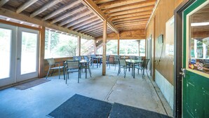 An outdoor covered patio with wooden beams, tables, chairs, and a door with a green frame.