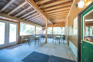 A covered outdoor seating area with tables and chairs, wooden beams, and a door with a green frame.
