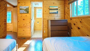 A cabin with wooden walls, two beds, a dresser, a painting, and a window.