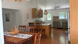 Zona pranzo con sedie e tavolo in legno, cucina con isola centrale e ventilatore a soffitto.
