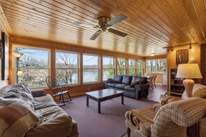 A spacious cabin with a wooden interior, large windows, a ceiling fan, and a cozy seating area.