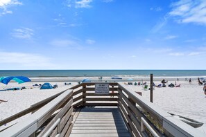 A wooden boardwalk leading to a beach with a 'DO NOT Leave Shoes or Personal Items on Boardwalk or Stairs' sign.