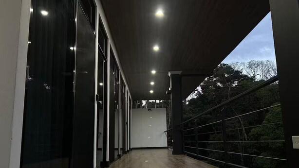 A corridor with glass doors, a wooden floor, and a view of trees. - Duke's Place 3 (Quepos)