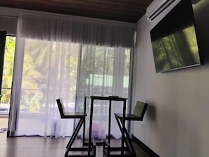Ein Zimmer mit großem Fenster, einem an der Wand montierten Fernseher und einem Tisch mit Stühlen.