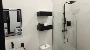 A modern bathroom with a wooden ceiling, a glass shower enclosure, a white toilet, a marble sink, and a black countertop. - Estudio Duke´s Place n.º 6 (Quepos)