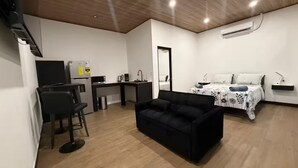 A compact living space with a kitchenette, a sofa, a bed with a floral bedspread, and a mirror. - Estudio Duke´s Place n.º 6 (Quepos)