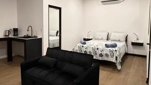 A modern room with a black sofa, a bed with patterned bedding, a desk with a mirror, and a ceiling with recessed lighting. - Estudio Duke´s Place n.º 6 (Quepos)