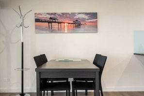 A dining area with a table and chairs, a floor lamp, and a sunset painting on the wall.