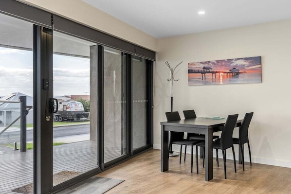 A dining area with a table and chairs, a painting on the wall, and a view through a glass door.