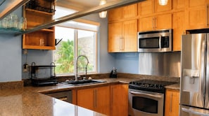 Une cuisine dotée de plans de travail en granit, d’armoires en bois, d’appareils électroménagers en acier inoxydable et d’une fenêtre donnant sur un paysage verdoyant.