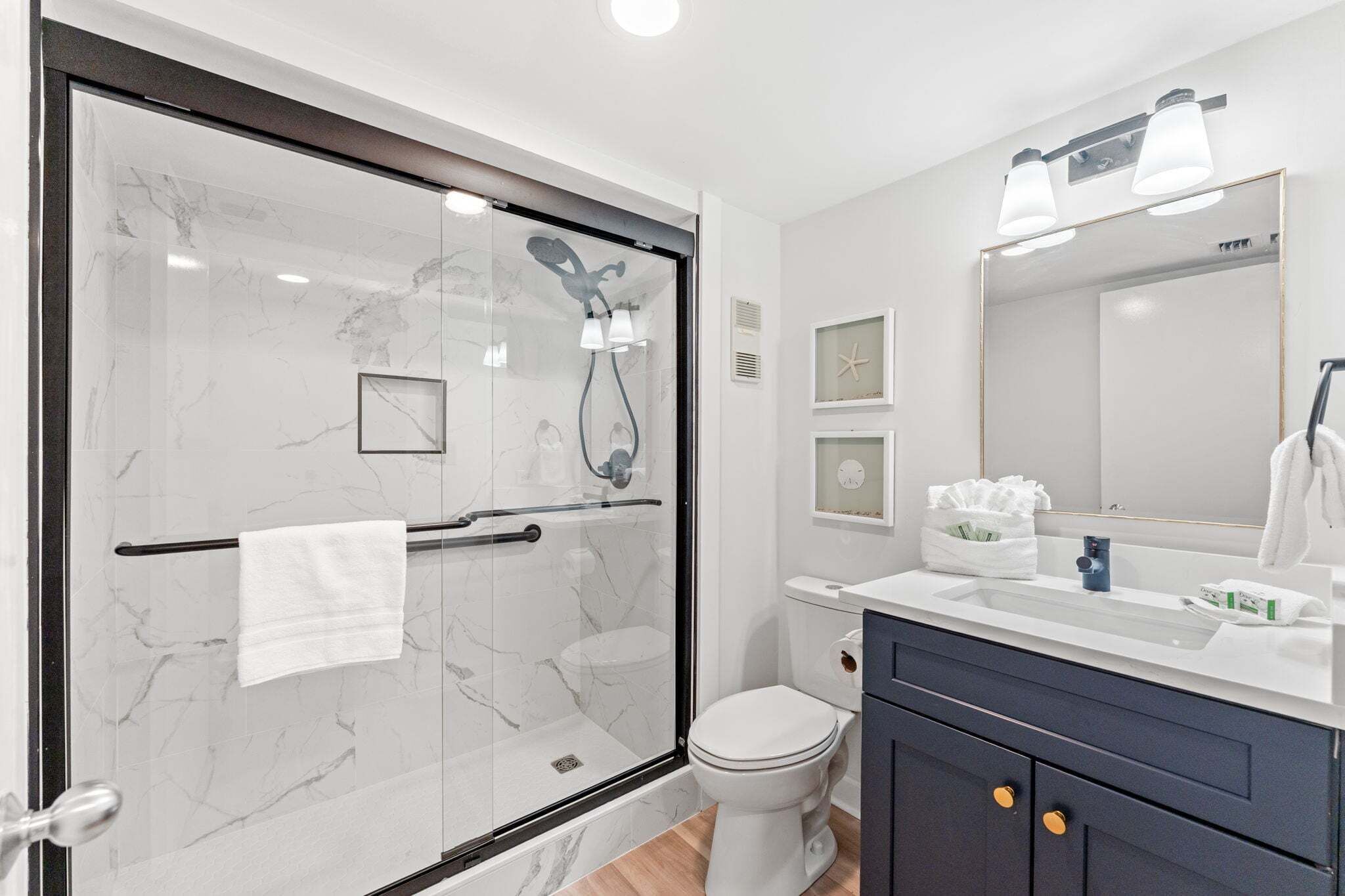 Un baño moderno con ducha de vidrio, inodoro blanco, tocador con espejo y barra para toallas.