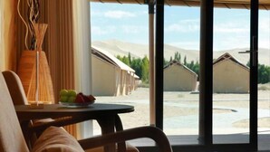 Une pièce dotée d’une grande porte-fenêtre coulissante, d’une table sur laquelle se trouve un panier de fruits et d’une chaise avec un coussin.