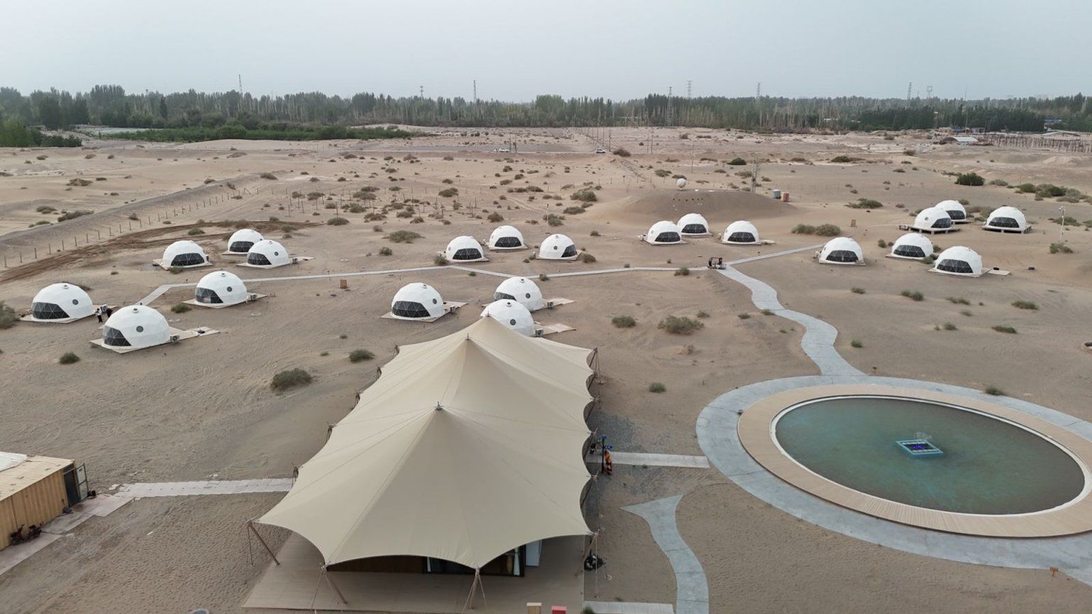 A desert landscape with multiple dome-shaped structures, a large tent, and a circular pool.