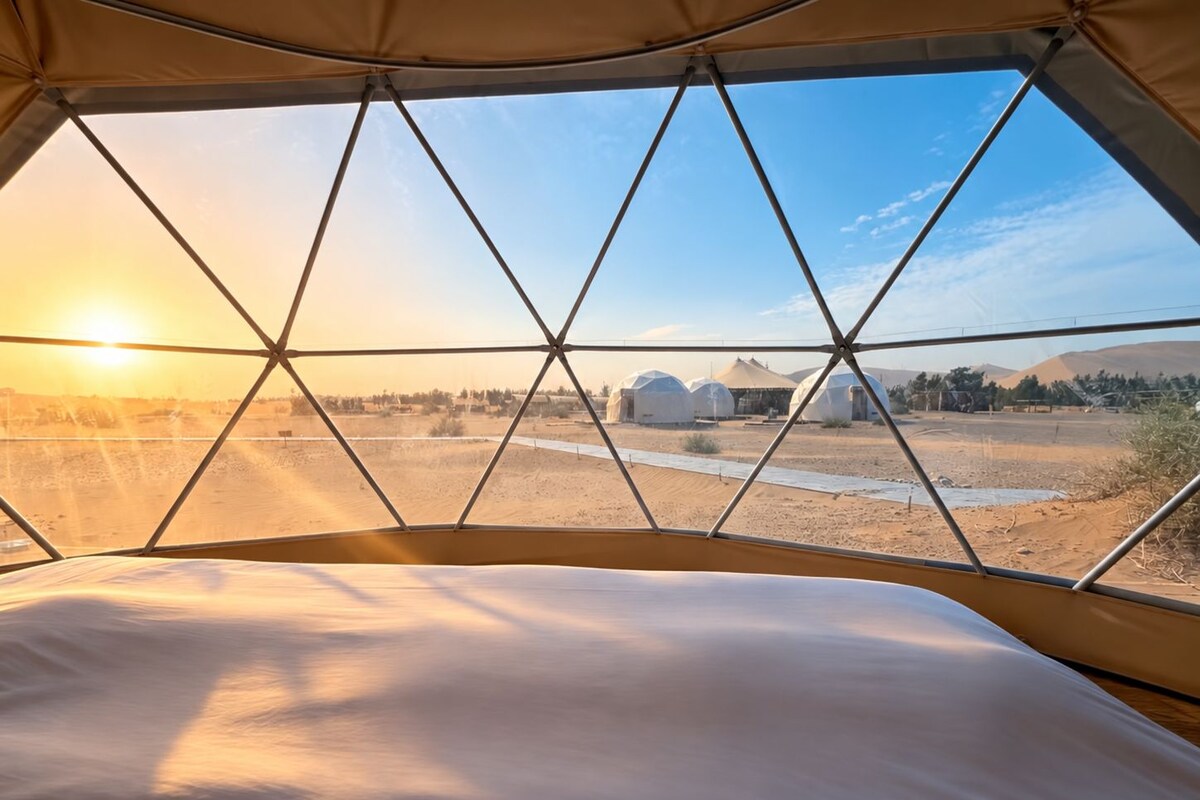 Uma tenda com vista para uma paisagem desértica e várias yurtas.