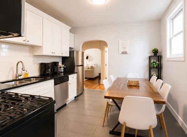 Une cuisine moderne avec des meubles blancs, un réfrigérateur en acier inoxydable et un coin repas comprenant une table en bois et des chaises blanches.