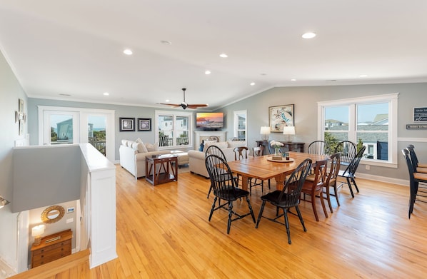 A spacious living area with a dining table, chairs, a sofa, and a fireplace. - Family Tree House | 2-Min Walk to Beach, Putting Green, Game Room & Large Fenced Yard (Holden Beach)