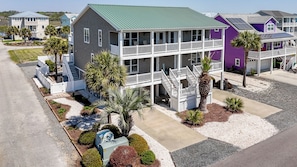 A two-story building with a green roof, white railings, and a covered front porch. - Family Tree House | 2-Min Walk to Beach, Putting Green, Game Room & Large Fenced Yard (Holden Beach)