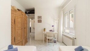 Quarto de hotel com cama, escrivaninha com cadeira, guarda-roupa e janela.