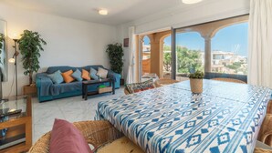 Uma sala de estar com sofá, mesa de jantar e vista através de um arco aberto.
