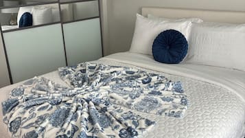 A bed with a quilted white cover, a blue floral throw blanket, and a single blue pillow.