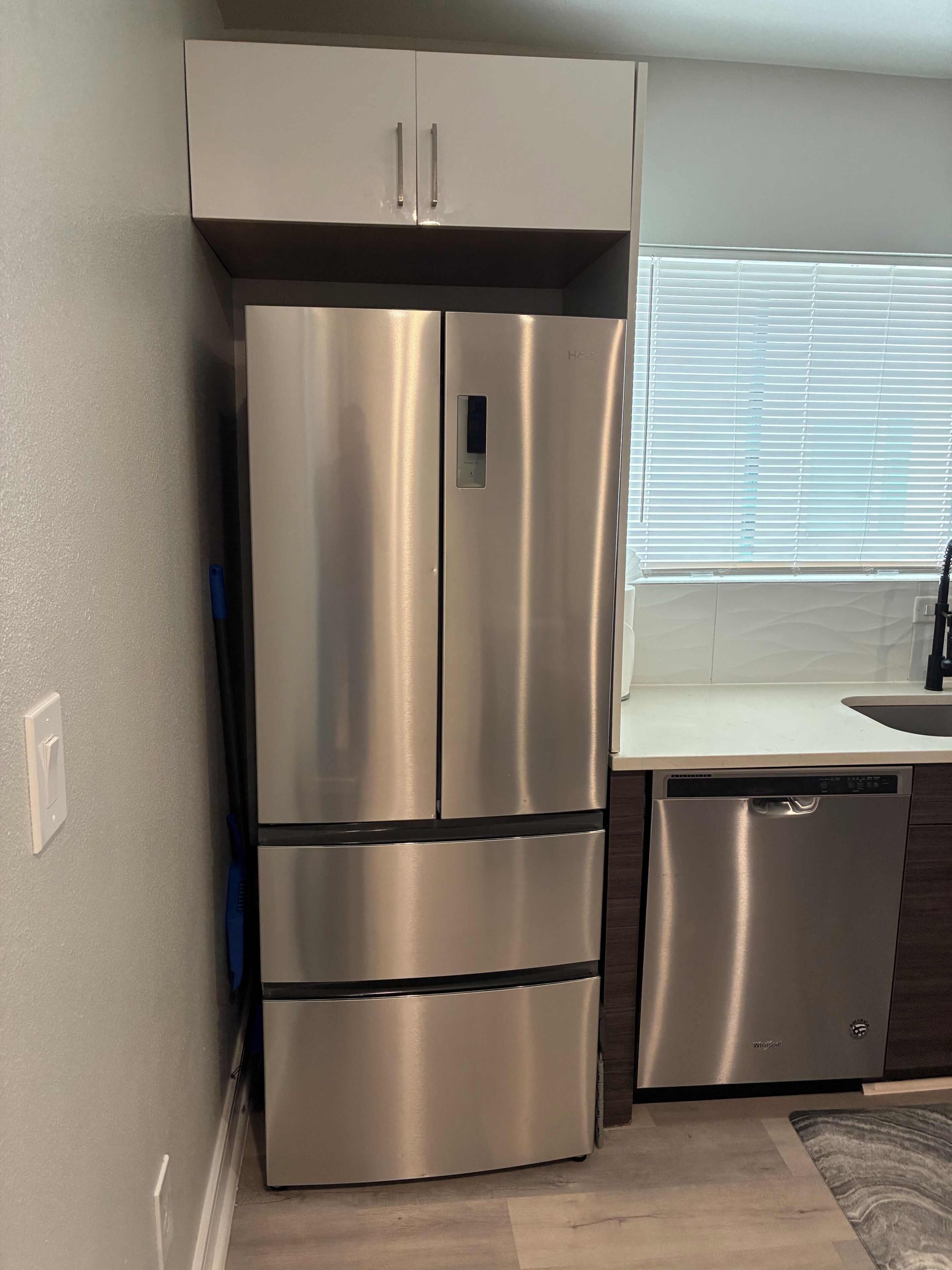 A stainless steel refrigerator with a built-in ice maker, a dishwasher, and a white countertop.