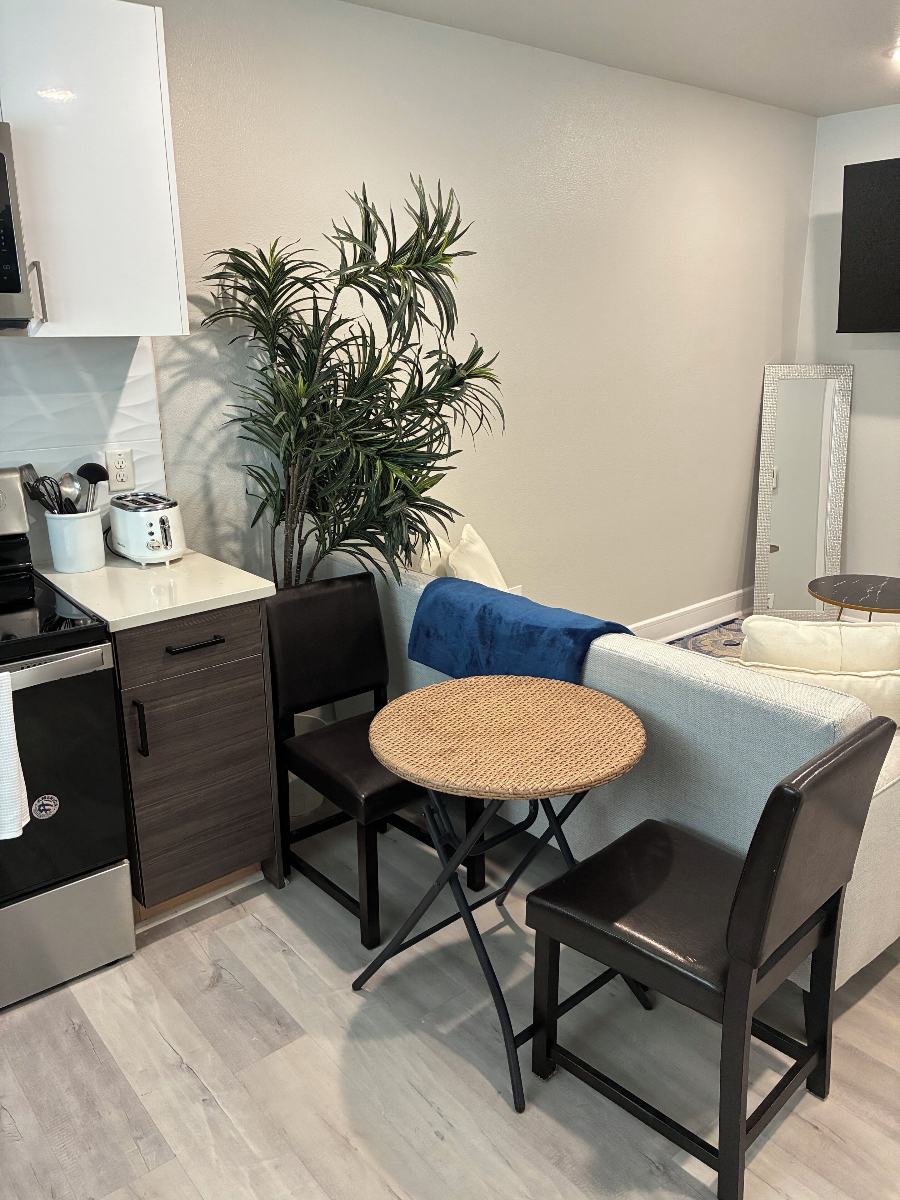 A compact kitchen with a toaster, a plant, and a dining area with a round table and chairs.