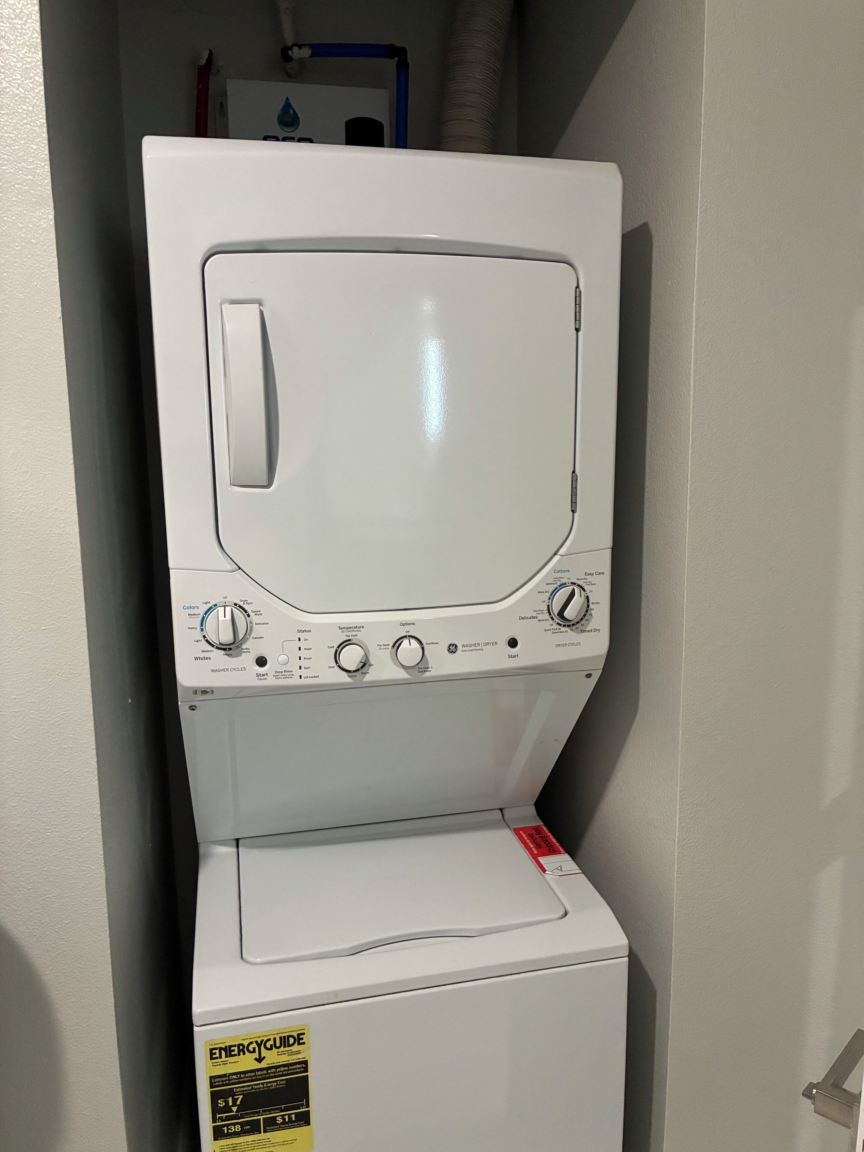 Een voorlader wasmachine met een bedieningspaneel, een rode sticker op de deur en een witte muur op de achtergrond.