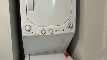Een voorlader wasmachine met een bedieningspaneel, een rode sticker op de deur en een witte muur op de achtergrond.