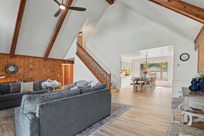 Un loft espacioso con techo alto, vigas de madera, una escalera, zona de comedor y sala de estar con sofá y reloj.