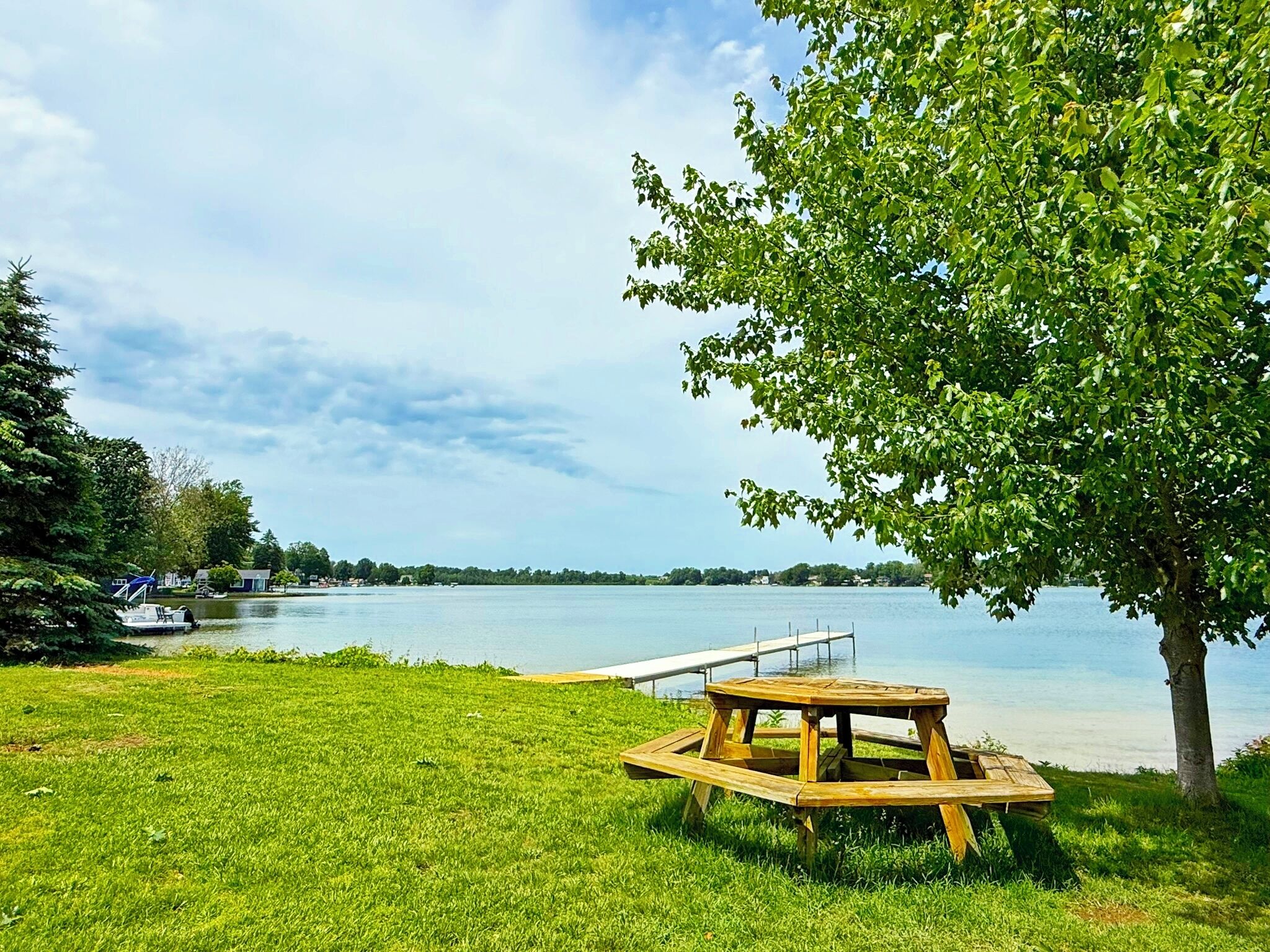 Zona verde con una mesa de picnic de madera y un muelle que se adentra en un lago.