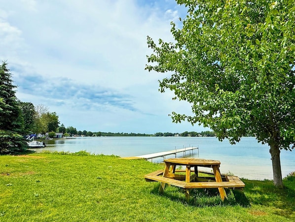 Zona verde con una mesa de picnic de madera y un muelle que se adentra en un lago.