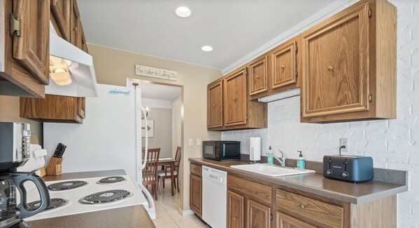 A kitchen with wooden cabinets, a white refrigerator, a microwave, a toaster, and a dining area with chairs and a table. - Vip Cabana at Abbey Villas- Steps to the pool (Fontana-on-Geneva Lake)