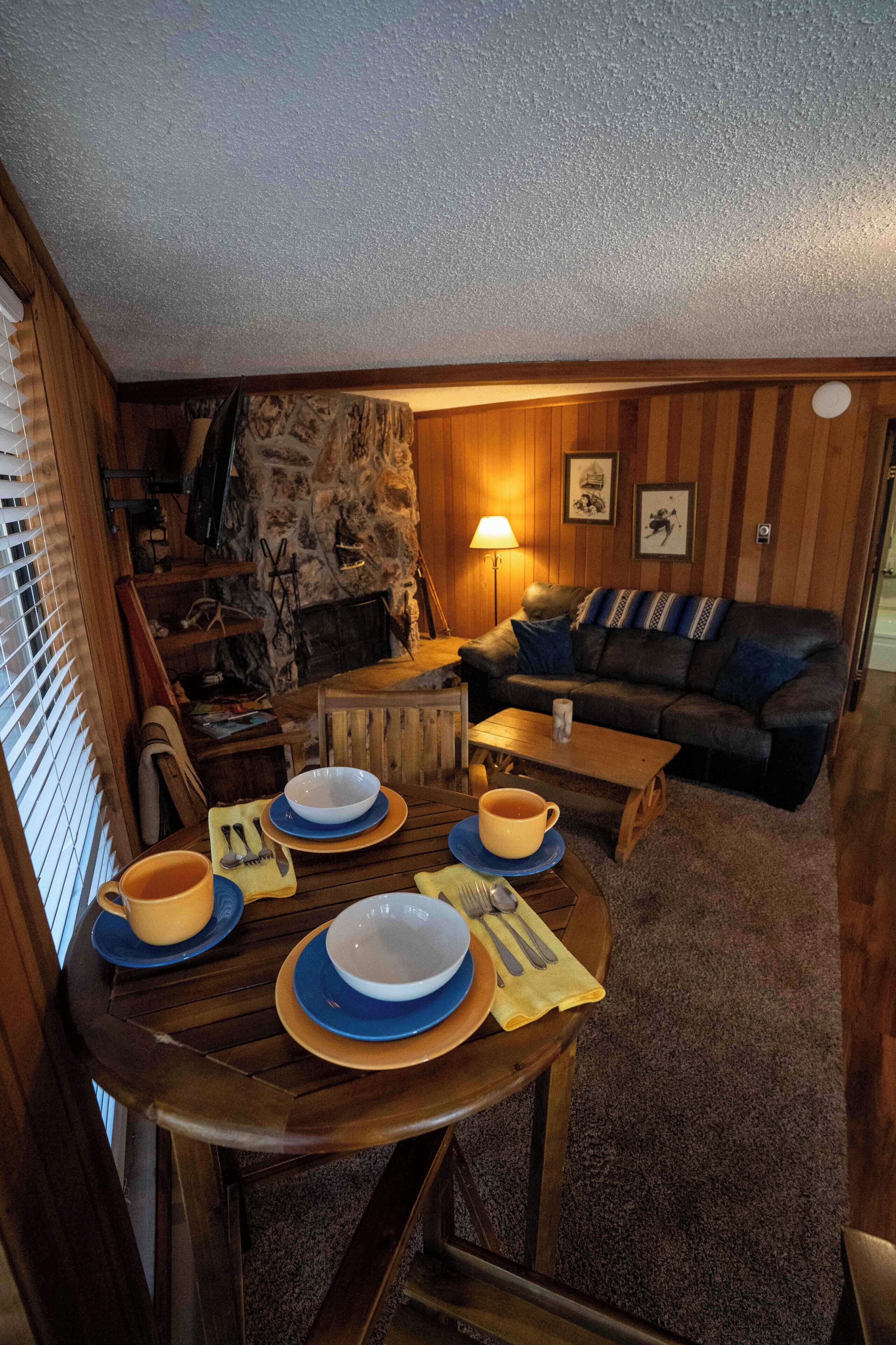 Un salon chaleureux avec une cheminée en pierre, des meubles en bois et un coin repas aménagé pour quatre personnes.