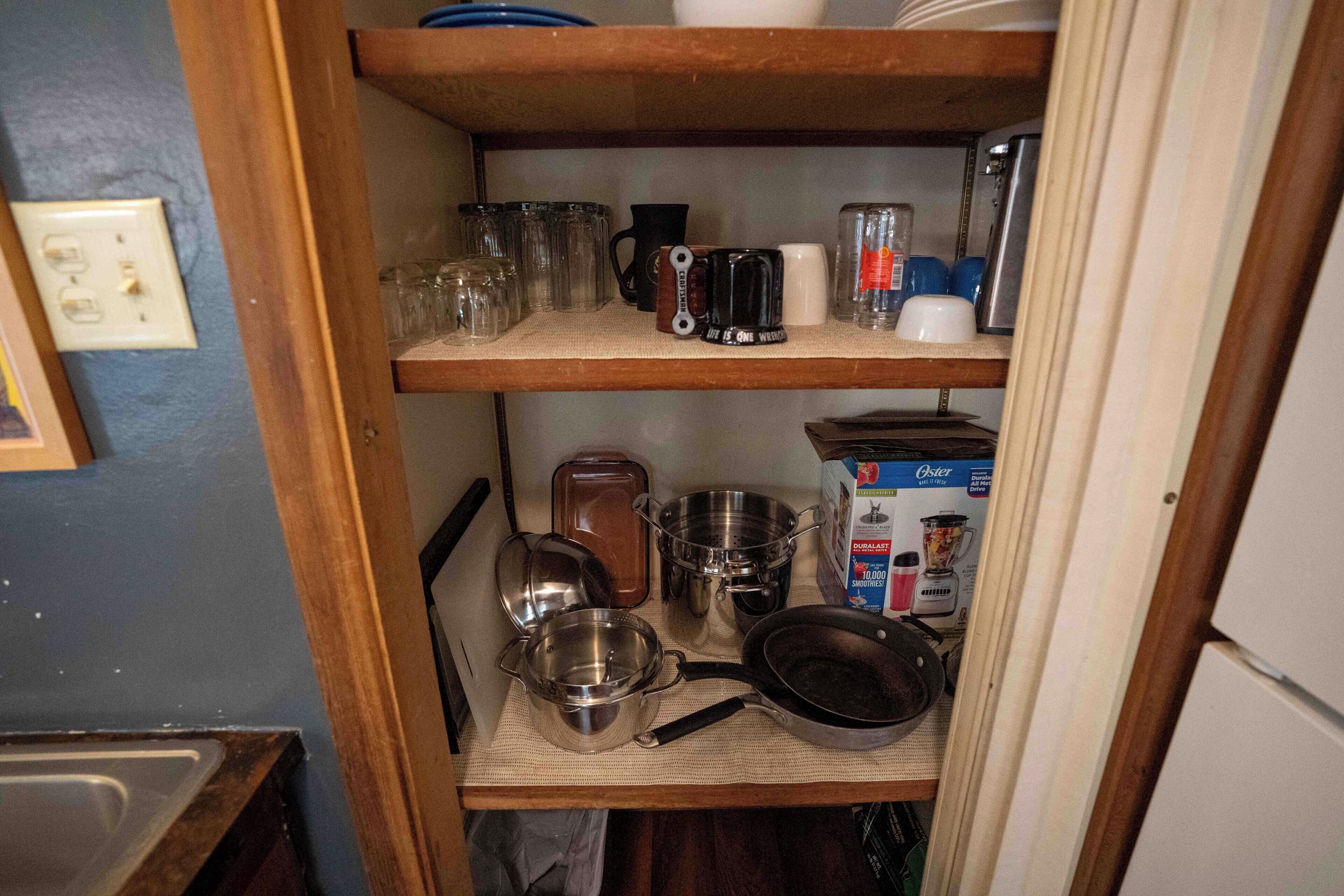 A kitchen shelf with various kitchenware, including pots, pans, and a coffee maker.