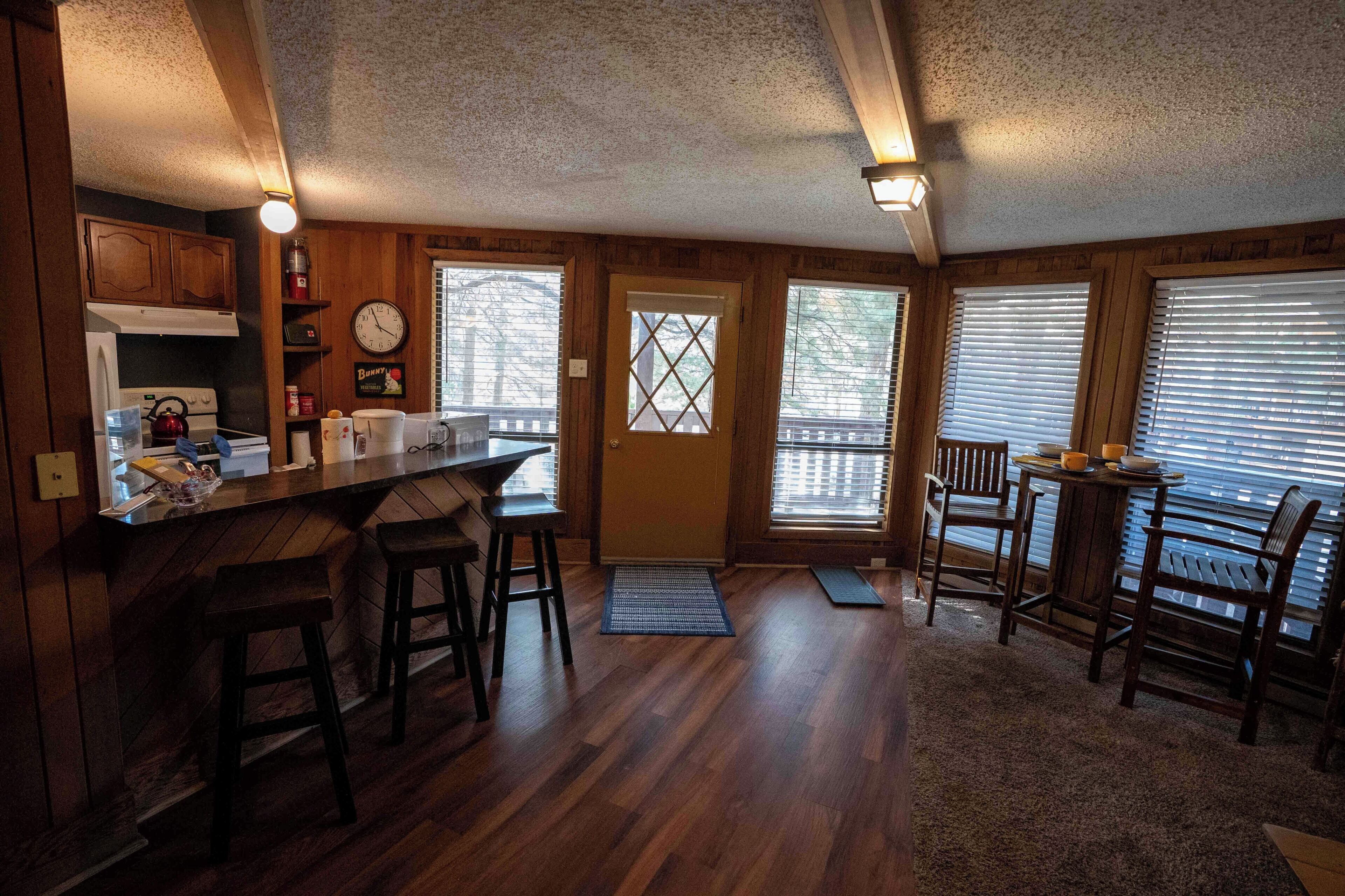 Une cuisine avec des meubles de rangement en bois, une cuisinière, un évier et un coin bar avec des tabourets.