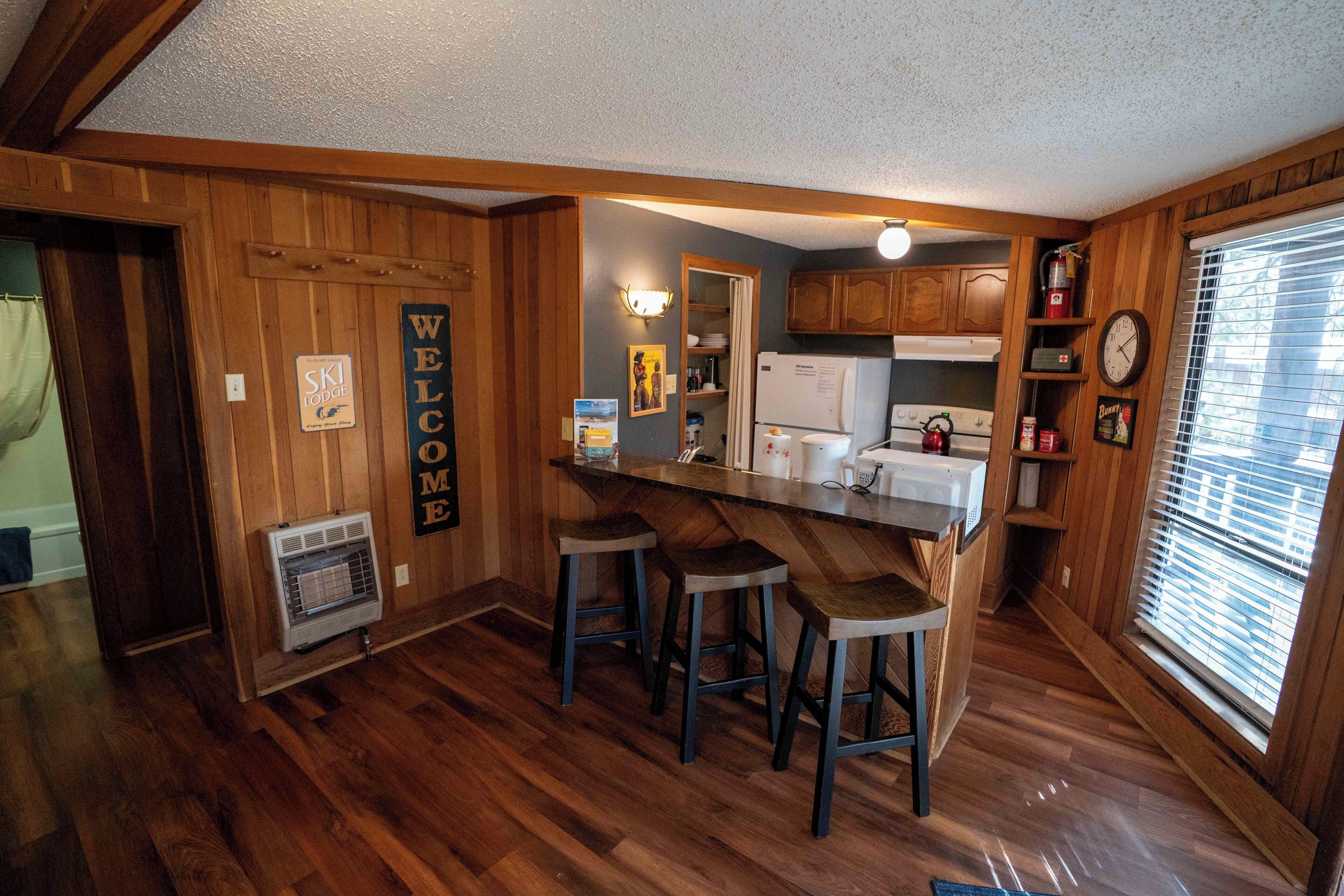Une cuisine avec des murs en bois, un coin bar avec des tabourets et une horloge au mur.