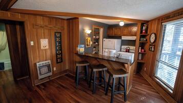 Une cuisine avec des murs en bois, un coin bar avec des tabourets et une horloge au mur.