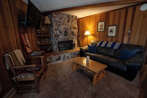 Ein gemütliches Wohnzimmer mit Kamin aus Stein, Holzwänden, einer Ledersofa und einem Couchtisch aus Holz.
