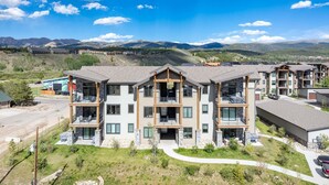 Un edificio de varios pisos con balcones, grandes ventanales y vista a las montañas.