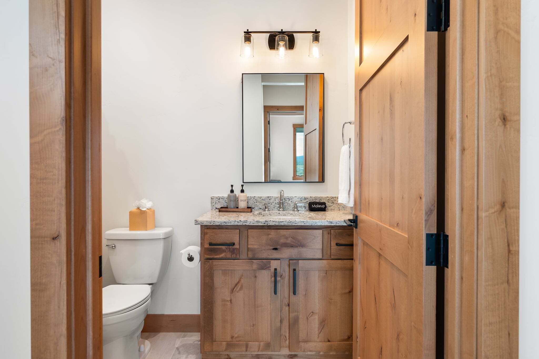 A bathroom with a toilet, wooden cabinets, a granite countertop, a mirror, and a towel rack.