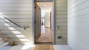 Entrada de una casa con el número '202' sobre la puerta, un felpudo que dice 'HAPPY HOME' y una escalera a la izquierda.