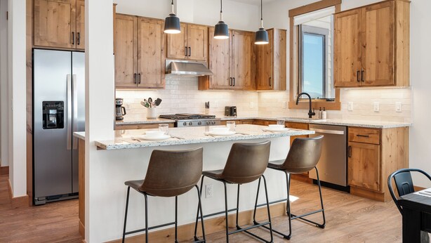 Una cocina moderna con armarios de madera, un refrigerador de acero inoxidable, una isla central con taburetes de bar e iluminación colgante.
