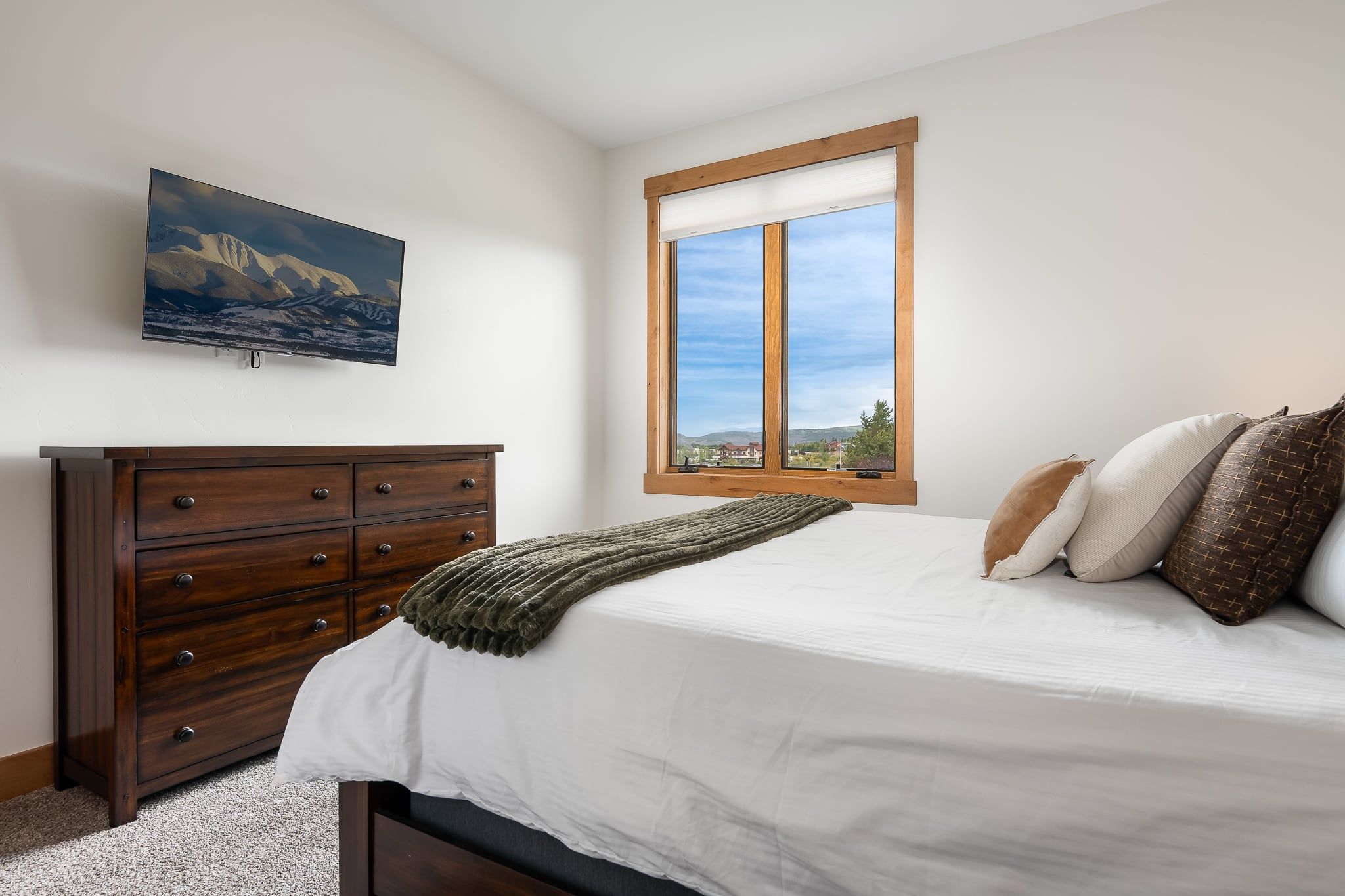 Une chambre à coucher avec un lit, une commode en bois, une fenêtre donnant sur un beau paysage et un tableau accroché au mur.