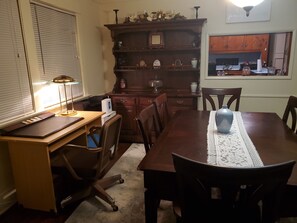 Ein Essbereich mit Holztisch, Stühlen, einer Lampe, einem Schreibtisch und einem Bücherregal.