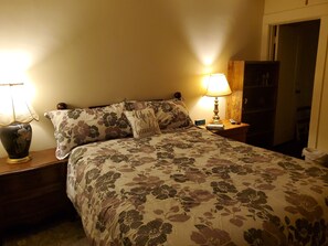 Ein Schlafzimmer mit Blumenmuster-Bettdecke, zwei Nachttischlampen, einem Nachttisch, einer Uhr und einem Kleiderschrank.