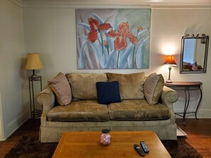 Ein Wohnzimmer mit Sofa, Couchtisch, Lampe, einem Gemälde und einem Spiegel.