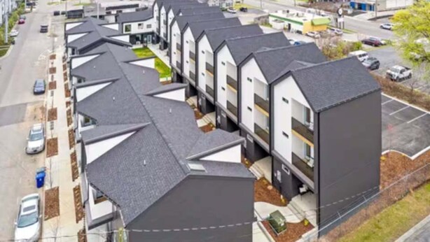 Una hilera de edificios residenciales modernos, de varios pisos y con techos inclinados, frente a un estacionamiento.