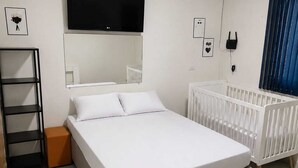 A bedroom with a bed, a TV, a crib, and a radiator.